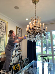 A professional cleaner from Vella carefully cleaning a chandelier inside a modern Austin home to improve indoor air quality.