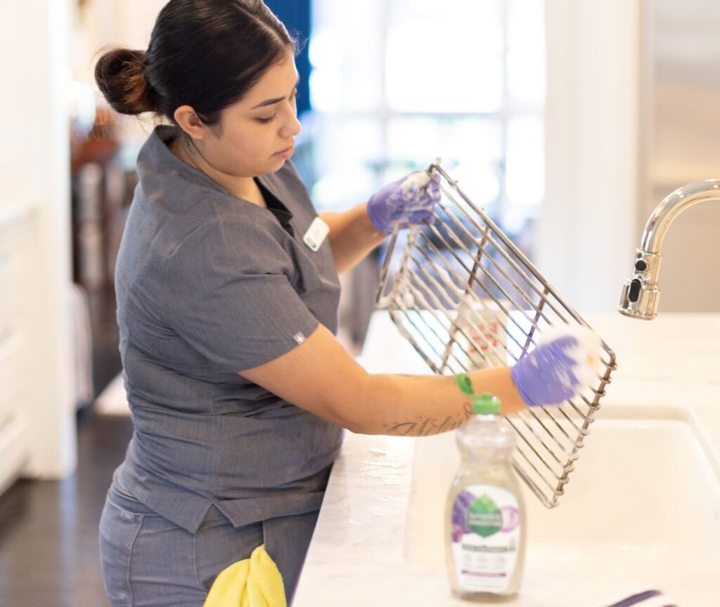"Professional cleaner scrubbing a kitchen rack over the sink "Professional cleaner scrubbing a kitchen rack over the sink, demonstrating effective techniques for cleaning your kitchen with eco-friendly products."