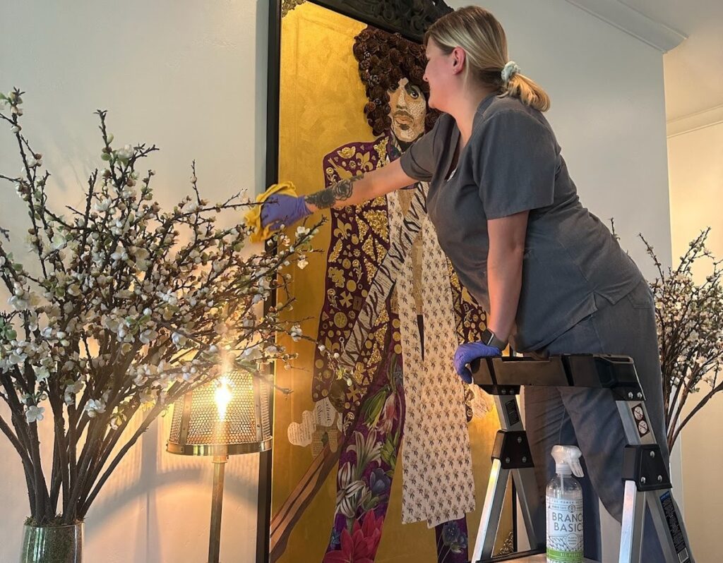 A cleaner standing on a step stool dusts intricate decor. A cleaner standing on a step stool dusts intricate decor, highlighting the attention to detail needed when you deep clean your kitchen and adjacent spaces.
