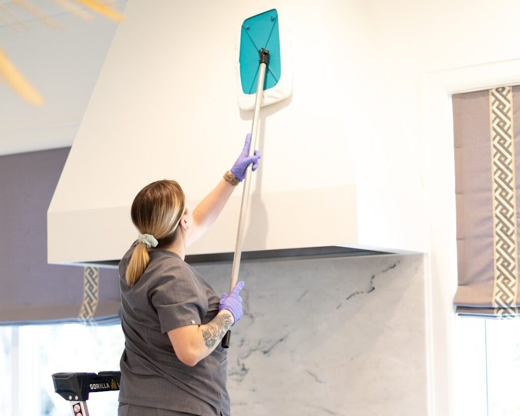 A cleaning professional using a tool to wipe a kitchen hood A cleaning professional using a tool to wipe a kitchen hood, highlighting the need to clean your kitchen hood effectively.