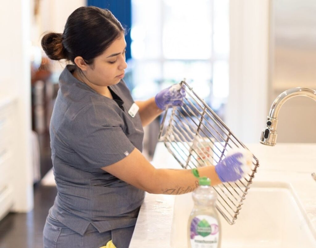 A professional cleaner scrubbing a metal rack A professional cleaner scrubbing a metal rack over a sink with soap and gloves.