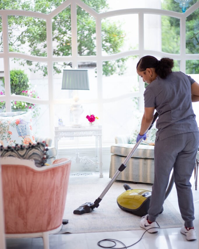 Vella cleaning professional in uniform vacuuming a living room floor.