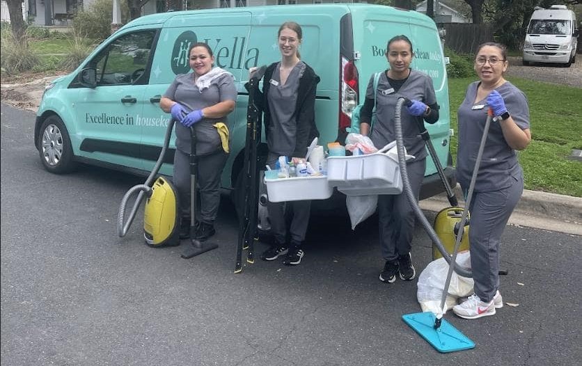 Housekeeping team with equipment in front of branded service van Housekeeping team standing in front of a teal van, equipped with cleaning tools including a vacuum and mop, ready for an assignment.