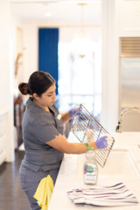 Housekeeper scrubbing an oven rack in a modern kitchen.