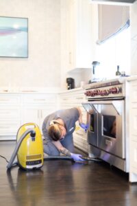 A Vella’s staff cleaning the dust and dirt from below the stove using a vacuum cleaning in Texas