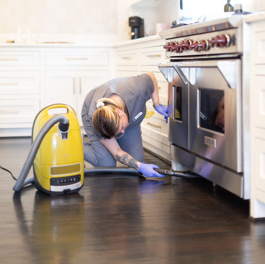 A Vella Housekeeper vacuuming below the oven A Vella Housekeeper vacuuming below the oven to ensure every single nook and cranny is completely clean.