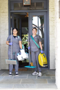 Two of Vella’s cleaning staff are standing in front of a Dallas home with all the cleaning supplies.