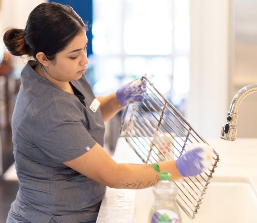 A professional cleaner wearing gloves is scrubbing a metal rack over a sink A professional cleaner wearing gloves is scrubbing a metal rack over a sink