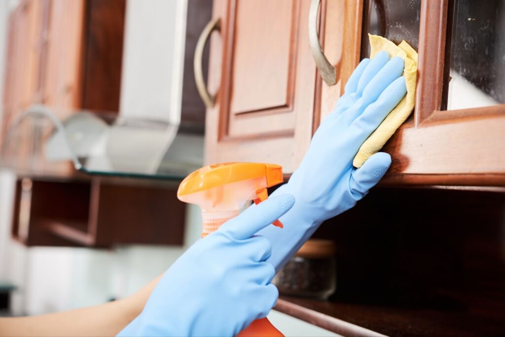 Gloved hands cleaning kitchen cabinets Gloved hands cleaning kitchen cabinets with a spray and cloth for a polished finish.