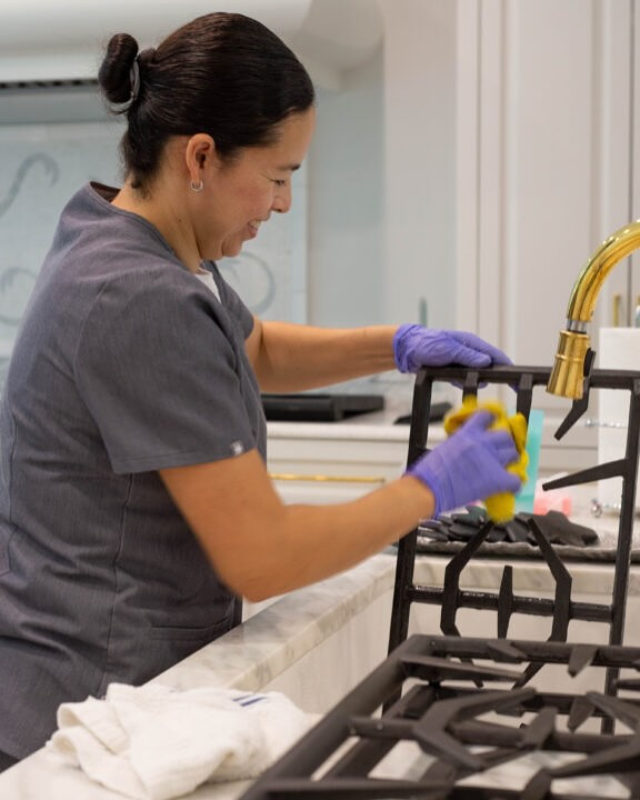 A Vella cleaner wiping a kitchen stovetop and fixtures with eco-friendly cleaning products in a Dallas home.
