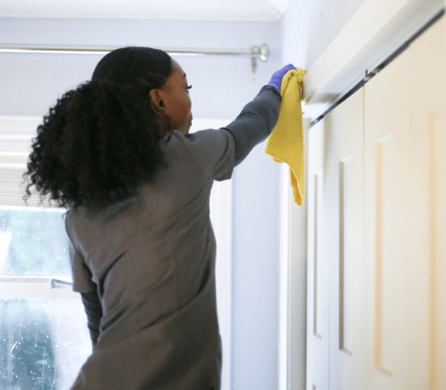 A professional cleaner in a grey uniform A professional cleaner in a grey uniform reaching up to dust window frames and door trim
providing thorough residential cleaning services at a client's home