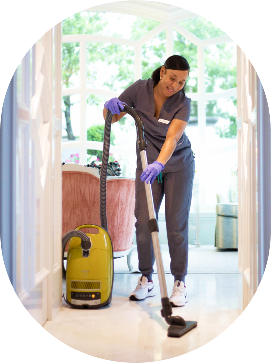 A Vella cleaning staff vacuuming the floor of the house wearing protective gloves.